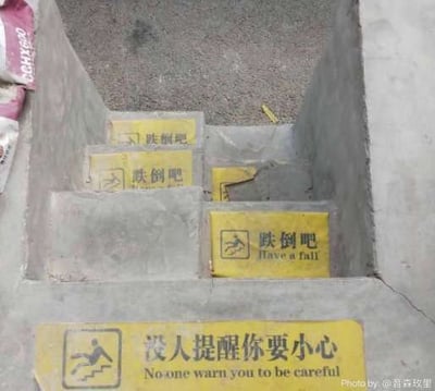 整张图为俯拍的水泥台阶实拍画面，台阶上共贴有多张黄底黑字的警示贴纸：最下方的台阶贴纸左侧印有行人从楼梯滑倒的简笔画标识，右侧配中文“没人提醒你要小心”，下方对应英文翻译存在语法错误，为“No one warn you to be careful”；其上方几级台阶的贴纸左侧原本应为提醒小心滑倒的标识，文字内容却被恶搞替换为“跌倒吧”，下方对应英文为“Have a fall”，完全违背了安全警示的原本意图，通过和常规提示语完全相反的语义制造出荒诞搞笑的效果。