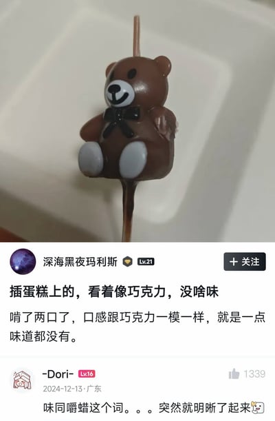 这是一张社交媒体帖子截图，图片上半部分展示了一个棕色小熊造型的物品，它被固定在签子上，外观和巧克力小熊棒棒糖几乎一模一样；下半部分是帖子文字内容，原帖作者“深海黑夜玛利斯”吐槽称这个物品是插在蛋糕上的，自己误以为是可食用巧克力，啃了两口后发现口感和巧克力相似，但完全没有味道；下方热评网友“-Dori-”评论点明笑点，称“味同嚼蜡这个词。。。突然就明晰了起来”，这个玩笑的核心是该物品实际是蛋糕装饰用的蜡烛，本身就是蜡，完美对应了“味同嚼蜡”的字面意思，产生了幽默效果。