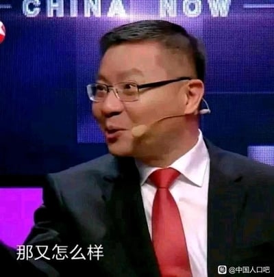 图片中是一位戴着眼镜、穿着深色西装和红色领带的男性，他佩戴着耳麦，似乎正在舞台或演播室中发言。背景为深蓝色，隐约可见“CHINA NOW”字样。人物表情自信，嘴角微扬，眼神看向一侧。图片底部有白色文字“那又怎么样”，传达出一种不屑或反问的语气。