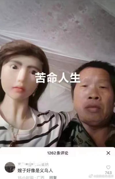 该图为社交媒体内容截图，上半部分是一名穿着迷彩上衣的中年男子的自拍画面，他手臂搭在身旁身着黑白条纹上衣的女性外形充气娃娃肩上，画面中间标注有白色文字“苦命人生”；下半部分是该内容的评论区片段，获赞743的高赞评论内容为“嫂子好像是义乌人”，用调侃的方式点出图中所谓的“嫂子”实际是义乌生产的充气玩具，暗指男子没有现实伴侣只能与充气娃娃相伴，玩梗效果十足，笑点荒诞诙谐。