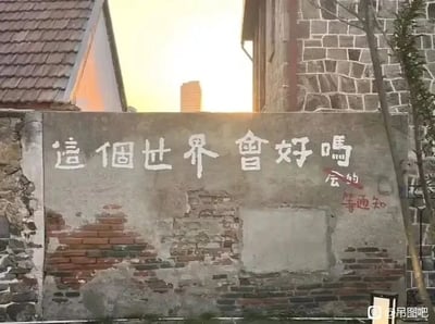 这是一张原始拍摄的静态单图，画面主体是一面老旧的水泥砖墙，墙面有多处破损，露出下方的红砖，显得颇有年代感。墙的后方是带有深灰色瓦片屋顶和石砌墙面的建筑，背景中夕阳散发着柔和的暖光，为画面增添了静谧的氛围。墙面上先用白色繁体字体写下“這個世界會好嗎”，之后有人用红色字体在问句下方补充了“会的”，还额外写下“等通知”，将原本带有迷茫、哲思意味的问句，用职场中常见的“等通知”来回应，形成了带有黑色幽默的调侃，暗指生活或职场中那种充满不确定性的等待状态，容易引发网友的共鸣。