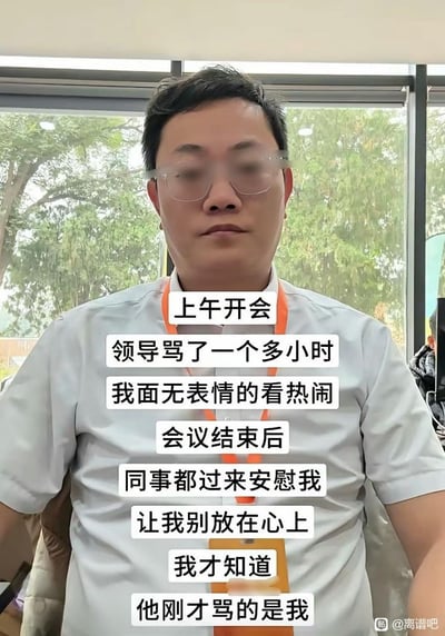 办公室场景中，一位戴眼镜、穿浅色衬衫的男性面无表情地坐着，背后是窗外的绿树。图中文字讲述了他上午开会时，领导骂了一个多小时，他面无表情地看热闹，会议结束后同事来安慰他，他才发现领导骂的是自己的社畜尴尬经历。