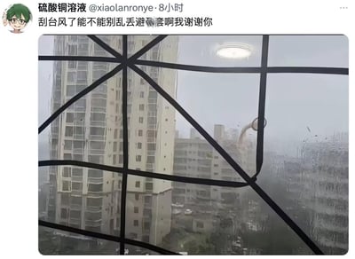 这是一则来自微博的社交媒体截图内容，发布者在台风天气里从室内窗边向外拍摄，窗外大雨倾盆，能见度较低，一栋高层建筑旁有个被强风吹得悬在半空的物品，因形状和视角巧合，看起来像被丢弃的避孕套。发布者因此配文吐槽“刮台风了能不能别乱丢避孕套啊我谢谢你”，制造出了搞笑的乌龙效果，实际上是典型的视觉错觉场景，并非真的有避孕套被丢弃。