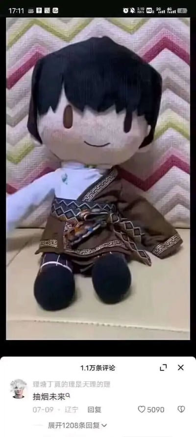 这是一张竖屏格式的社交媒体截图，整体分为上下两个区域。上半部分是一个模仿网红理塘丁真形象制作的毛绒玩偶，玩偶有着齐整的黑色短发，面部带着温和的微笑，身着带有民族风格纹样的棕色外搭与白色内搭，以端正的坐姿放置在带有彩色锯齿纹的背景前；下半部分是该内容的评论区界面，界面顶部显示共有1.1万条评论，置顶的热评来自用户“理塘丁真的理是天理的理”，发布内容为“抽烟未来😮‍💨”，发布时间标注为07-09，地点显示为辽宁，这条评论收获了5090个点赞，还可展开查看1208条回复，评论内容是结合原神相关元素的谐音玩梗。