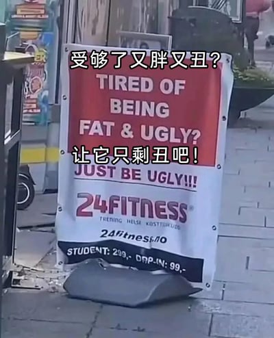 这是一张户外实拍的24FITNESS健身房宣传广告牌，放置在铺有石板的街道地面上。广告牌以红白色为主色调，上方用醒目的大号英文字体写着极具冲击力的文案“TIRED OF BEING FAT & UGLY? JUST BE UGLY!!!”，下方标注了健身房品牌名“24FITNESS”，还有挪威语文字“TRENING HELSE KOSTTILSKUDD”（意为训练、健康、营养补充剂），以及品牌官网地址“24fitness.no”和收费信息：学生月费299，单次入场99（未标明具体货币单位）。图片上叠加了简体中文翻译文字：“受够了又胖又丑？让它只剩丑吧！”，将英文文案的扎心感精准传达。这种反常规的自嘲式营销文案，没有用常见的“变瘦变美”这类正向宣传，而是用放大焦虑的反向话术，显得格外搞笑接地气，以此吸引有减肥需求的潜在客户。背景中右上角能看到模糊的行人身影，整体场景是日常的户外街道环境。