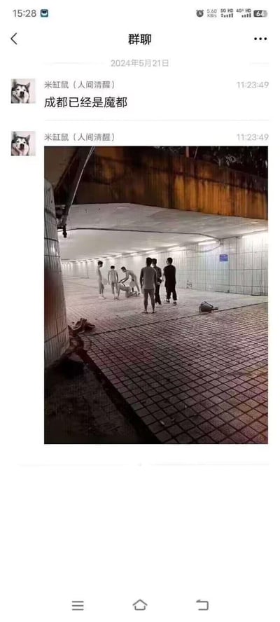 这是一张2024年5月21日的微信聊天群截图，群成员“米缸鼠（人间清醒）”在11:23:49同步发送了文字“成都已经是魔都”与一张实拍照片。照片呈现的是一处明亮的地下通道场景，地面铺着方格地砖且带有水渍，几名男子聚集在通道中央，部分人脱去上衣，其中一人正蹲身照料地上的人，旁侧还放置着衣物包袋。配文中的“魔都”本是上海的代称，此处用来调侃成都天气极端炎热，热到出现需要救助的状况，将成都的高温夸张地类比成“魔都”的特殊状况。