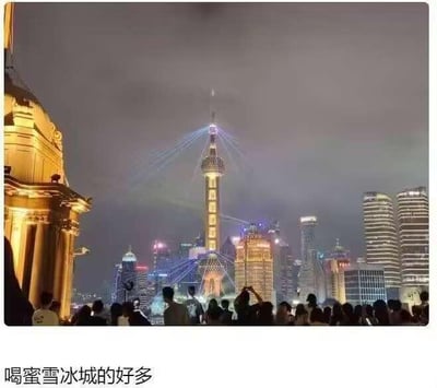 这是一张夜晚拍摄的上海外滩观景区域的照片，画面左侧是外滩的古典欧式建筑，对岸陆家嘴的东方明珠广播电视塔亮起暖黄色灯光，多束蓝色激光从塔上射出，指向聚集在观景台的大量人群。图片下方配有文字“喝蜜雪冰城的好多”，是玩了视觉联想梗：东方明珠的暖黄色塔身形似蜜雪冰城的奶茶杯，射出的激光像奶茶吸管，结合聚集的人群，仿佛是很多人在“喝”这个巨型蜜雪冰城奶茶，制造出搞笑的趣味效果。
