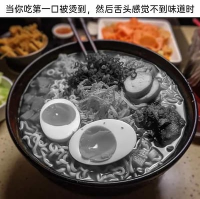 这是一张基于生活体验创作的搞笑P图，图中原本色泽丰富的拉面，其面、溏心蛋、肉片等主体部分被处理为黑白色调，而背景里的配菜小食仍保留正常彩色；图片上方配有文字“当你吃第一口被烫到，然后舌头感觉不到味道时”，用视觉上的“失色”来比喻舌头被烫后味觉丧失、吃什么都没有滋味的状态，生动又形象地还原了那种无奈又好笑的日常经历。