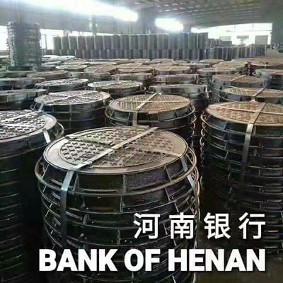 图片展示了一个工厂仓库内大量堆放的圆形井盖，这些井盖整齐地堆叠在一起，形成密集的排列。图片下方有醒目的文字“河南银行”和对应的英文翻译“BANK OF HENAN”。

该图片使用了双关和暗示手法，在中国网络文化中，“井盖”与“河南”存在特定的调侃关联，这里通过将银行名称与大量井盖并置，形成了对河南银行的幽默讽刺。