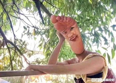 图片中展示了一张经过趣味P图处理的场景：一名人物的头部被替换成一只脚的形状，脚部皮肤纹理清晰可见，脚趾微微弯曲，脸上还带着明显的微笑表情。人物身体穿着带有花纹的衣服，单臂撑在栏杆上，背景是茂密的绿色树叶和树枝，阳光透过叶缝洒下，整体画面充满滑稽荒诞的幽默感。