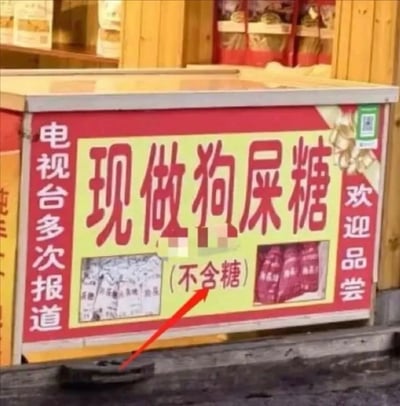 这是一张非常魔性又搞笑的中国地方小吃摊广告照片。牌子上写着“现做狗尿糖（不含糖）”，用极为大胆直白的宣传方式吸引眼球。狗尿糖其实是麦芽糖的一种别称，不过因为字面意思非常冲击，常常引起外地游客误会或发笑。下面还特地标注“（不含糖）”，极具喜感。整体风格土味、幽默，成为网友争相转发的魔性表情包。该图片无明显双关与谐音梗，但名称本身带有强烈暗示效果和低级趣味。