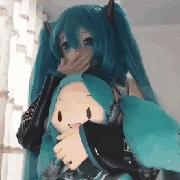 这是一段温馨可爱的动态GIF，画面中的真人coser完美还原了虚拟歌手初音未来的标志性蓝绿色双马尾与造型服饰，她用一只手捂着嘴，露出偷笑的神情，另一只手紧紧抱着一个Q版初音未来玩偶，玩偶被温柔地搂在怀中，整体画面充满了粉丝对虚拟角色的喜爱与亲切感，氛围轻松治愈。