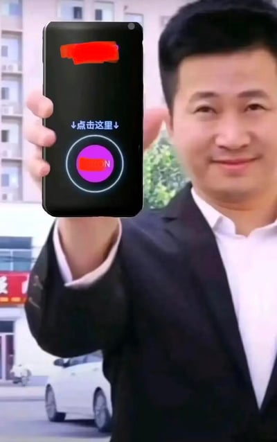 这是一张经过图像合成改编的图片，将演员吴京的面部合成到一位身着黑色西装、白色衬衫的男性身体上。该男性抬手举着手机，手机屏幕显示“↓点击这里↓”的引导文字，下方配有一个紫色圆形按钮，按钮上的文字被红色色块遮挡。背景是户外街道场景，可见建筑物、车辆等元素，整体呈现出类似引导点击的引流类内容，无谐音梗或双关含义。