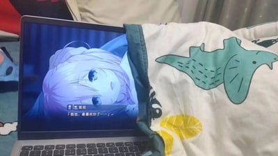 这是一张充满创意的实拍照片，画面里一台笔记本电脑的屏幕显示着美少女游戏《星光咖啡馆与死神之蝶》的剧情场景，角色紫苑正说出告白台词。一条印有绿色鳄鱼、黄色叶子图案的白色被子的边缘恰好衔接在电脑屏幕右侧，利用视觉错位的效果，让观看者产生游戏角色紫苑正盖着这条被子的错觉，将虚拟游戏场景与现实物品巧妙结合，营造出温馨又有趣的氛围，是玩家发挥创意的趣味互动。