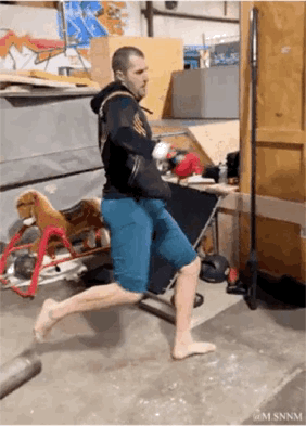 这是一段搞笑GIF动态图，画面中的男子身处堆满工具和杂物的工作室中，他将假肢固定在地面，另一条腿抬起做出跑步的动作，同时身体配合摆动，营造出原地跑步的假象，整个动作充满滑稽感，是典型的生活整活搞怪内容，让人看后忍俊不禁。