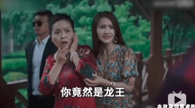 图片为网络热梗'龙王赘婿'系列广告的经典截图。画面中，一位身穿红色传统服饰的中年女性双手捂嘴，面露极度震惊表情，身体微微后倾；旁边一位穿着碎花连衣裙的年轻女性伸手搀扶着她，同样面露惊讶。背景中站着一位戴墨镜的男性，表情冷峻。画面底部有白色字幕'你竟然是龙王'，这是该系列广告中'身份揭露'环节的标志性台词，展现了'卑微赘婿突然暴露龙王身份，众人震惊'的爽文式剧情高潮。