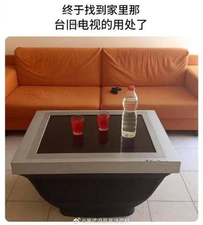 图片展示了一个创意家居改造场景：客厅中，一台旧电视被巧妙改造成了一张茶几，电视屏幕部分作为光滑的桌面，下方保留了电视原有的结构作为桌腿。茶几上摆放着两个红色玻璃杯和一瓶矿泉水，背景是一张橙色的皮质沙发，沙发上放着一个黑色遥控器。图片上方配有文字“终于找到家里那台旧电视的用处了”，突出了旧物改造的实用性和创意性，给人一种变废为宝的惊喜感。