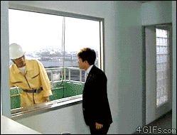 这是一则利用视觉错位效果的搞笑动态GIF。画面中，室内一名身着黑色西装的男子正站在窗边，看向窗外一名穿着黄色工装、戴着白色安全帽的施工工人，工人的位置看起来像是紧贴在高楼窗户的外侧，给人一种随时会坠落的错觉。下一秒，工人突然向下‘坠落’，实际上工人是站在高楼外侧向下延伸的平台上，并非窗户的垂直外侧，视角差制造出了工人从高楼坠落的假象，反差感拉满，十分滑稽。