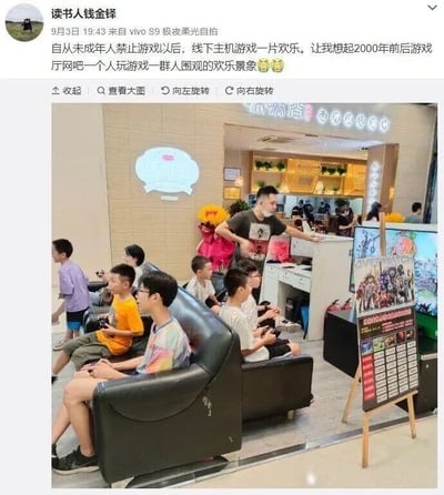 这是一张微博截图，发布者为用户“读书人钱金铎”，发布时间为9月3日19:43，发布设备为vivo S9。微博文字内容提到在未成年人游戏限制政策实施后，线下主机游戏场所变得十分热闹，让人回想起2000年前后游戏厅、网吧里一人玩游戏众人围观的欢乐场景，并配有两个开心的表情。截图下方的实拍照片展示了一家名为“嗨潮窝”的线下主机游戏店铺内的场景：一群未成年人坐在黑色皮沙发上，手持游戏手柄专注地玩着主机游戏，部分孩子身旁还有人围观；一位戴着口罩的成年人站在柜台旁，伸手做出服务或引导的动作；店铺内还有其他顾客，一旁立着游戏宣传立牌，整体氛围热闹，完美呼应了微博文字描述的内容，重现了早年游戏场所的围观欢乐景象。