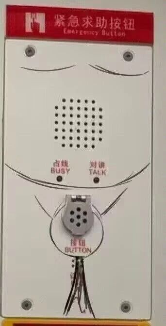 这是一张经过涂鸦改编的静态原始拍摄图，主体是一个安装在墙面上的白色紧急求助按钮设备。设备顶部有红色的标识牌，写有“紧急求助按钮 Emergency Button”字样。有人用黑色涂鸦在设备上进行了创意创作：在设备上方绘制了两道眉毛，将设备中间的出声孔区域对应为人脸的鼻子，下方的“占线BUSY”“对讲TALK”指示灯对应脸颊，底部的圆形按钮区域被涂鸦出嘴部的轮廓，还在按钮下方画了类似领带的图案，让原本严肃的应急设备看起来像一个佩戴领带的人脸，充满了诙谐的恶搞趣味，属于对日常公共设施的趣味二次创作。
