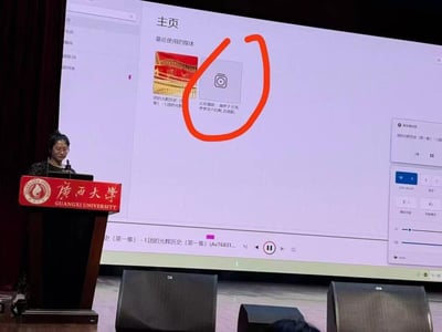 这是广西大学一场正式的校园宣讲活动现场，一位女教师正在讲台上发言，身后的大屏幕展示着媒体播放软件的界面，其中「最近使用的媒体」栏里出现了标题包含低俗色情内容的视频，与正在播放的严肃团史内容形成强烈反差，场面极度尴尬，属于典型的社死现场。