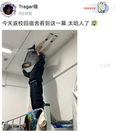 社交媒体用户Tragar翔发布的返校宿舍场景：一名学生站在宿舍床上，双手向上伸展，天花板处倒挂着另一名穿着运动鞋的人的双腿，营造出诡异惊悚的视觉效果。配文'今天返校回宿舍看到这一幕 太哈人了😱'表达了惊吓情绪，推测是宿舍同学间的恶作剧，引发网友共鸣。