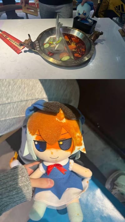 上图展示了餐桌上的鸳鸯火锅，清汤锅底漂浮着黄瓜片等食材，红汤锅底则布满辣椒和花椒，旁边还有一个蓝色头发的小玩偶摆件；下图特写一个橙发玩偶，其头部和额头沾满了红油，表情愤怒，仿佛在控诉自己掉进了火锅里。两张图形成有趣对比，记录了吃火锅时玩偶意外沾到红油的搞笑瞬间。