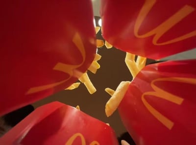 这是一张充满创意的低角度摄影作品，画面中四个带有麦当劳经典金色M标志的红色薯条盒，从画面的四个方向向中心‘展开’，散落的薯条从盒中伸出，借助视觉错位的效果，让原本普通的薯条盒看起来像是张开的‘大嘴’，薯条则如同牙齿，将日常的美食包装玩出了新奇的趣味感，十分吸睛。