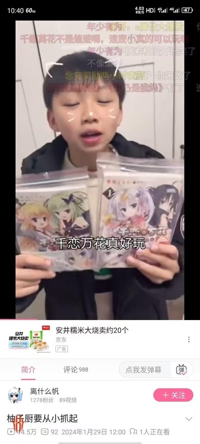 图片为竖屏手机格式的视频截图，画面中心是一名少年，脸颊有白色印记，闭眼张口，双手各持一袋印有动漫女性角色的周边商品。商品包装上可见“千恋万花”字样及绿发、紫发等动漫人物形象。画面上方覆盖大量黄色、红色弹幕式评论，内容包括“千恋万花不是渣男啊，追直也卖的可以书”“年少轻狂：s属性大爆发”“念完奖励两小时农孩子 你无敌了”等。底部显示视频发布者信息：账号“离什么帆”，1278粉丝，89个视频，发布时间2024年1月29日12:00，下方有京东“安井糯米大烧卖”广告及“评论988”“点我发弹幕”等交互按钮。