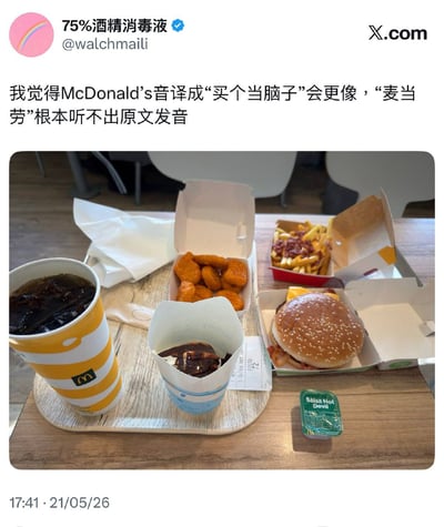 整张图是X平台的社交媒体动态截图，顶部显示发布者头像、用户名“75%酒精消毒液”、账号@walchmaili及平台标识，发布文案调侃麦当劳的中文音译，称将McDonald's音译为“买个当脑子”比官方译名“麦当劳”更贴近英文原发音，属于谐音梗趣味吐槽；下方配图是在麦当劳门店内拍摄的餐品，木质桌面上摆放着麦当劳的可乐、麦乐鸡、巧克力新地、汉堡、加配料的薯条，还有小盒辣酱和用餐小票，是典型的麦当劳堂食场景。