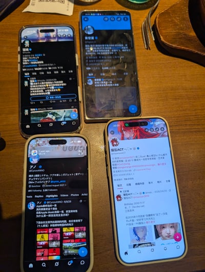 这张实拍照片拍摄于平价连锁西餐品牌萨莉亚的门店内，桌面为木质餐桌，桌上摆放了四部智能手机，每部手机都打开了X（原推特）平台的个人主页，对应四位参与本次线下面基的网友的账号，桌面还露出了餐具、消费小票的边角，是同好网友线下聚会时的趣味记录，以同时展示各自社交平台主页的方式彰显同好身份。