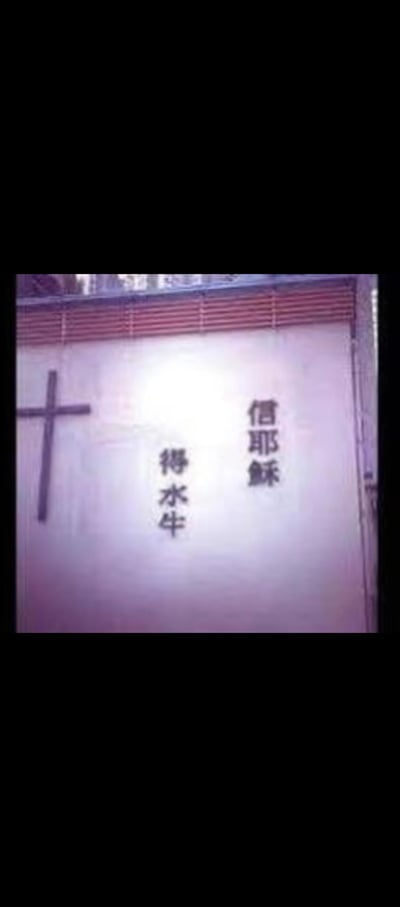 这是一张竖版拍摄的墙面标语图，墙面左侧绘制有基督教十字架标识，右侧竖排书写着“信耶稣”，其下方对应写着“得水牛”。该内容玩了谐音梗，将基督教经典传教语“信耶稣得永生”中的“永生”替换为“水牛”，用接地气的乡土词汇替换宗教概念，制造出强烈的荒诞反差感，十分搞笑。