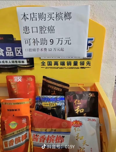 这是一张在槟榔售卖点拍摄的实拍图，黄色的槟榔展示架上陈列着多款不同价位的槟榔产品，涵盖10元、30元、50元档位，包括酱香槟榔、仁和天成等品牌。展示架上方贴着一张醒目的手写告示，内容为“本店购买槟榔 患口腔癌 可补助9万元”，下方还标注“口腔癌手术费12万元起”，用黑色幽默的反讽方式，直指槟榔会导致口腔癌的健康危害。同时展示架上还有“禁止向未成年人销售槟榔”“全国高端销量领先”等官方宣传语，与手写告示形成强烈反差，凸显讽刺效果。