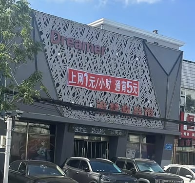 这张图片拍摄的是一家名为“Dreamer”的网吧门头，正中央悬挂着大红色的横幅广告：“上网1元/小时 通宵5元”。较为显眼的“Dreamer”英文名搭配极低的上网价格，有一丝“梦想与现实落差”的幽默感，在社交网络中常被调侃为“平价梦想空间、打工人的乌托邦”。图片中也含有双关/暗示氛围：高大上的英文名配上地摊价，表现出反差萌，经常引发网友玩梗：‘Dreamer’成了“只敢做梦”的象征。