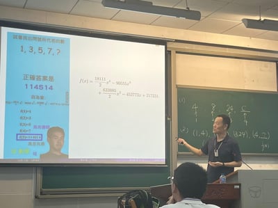 这是一张大学线性代数课堂的实拍图，讲台上的老师正在讲解内容，投影屏幕上展示了一个整活的数列题：给出数列1,3,5,7,?，却给出了离谱的“标准答案”114514，并用一个四次多项式f(x)来佐证——当x取1到4时，多项式结果分别对应数列的前四项，x=5时得到114514。屏幕右下角还配上了野兽先辈的表情包，用数学插值的严谨形式包装亚文化梗，制造出荒诞搞笑的反差感。

额外说明：114514是inm（淫梦）圈的经典数字梗，源于日本GV《真夏の夜の淫夢》中野兽先辈的台词谐音，属于小众亚文化网络梗。