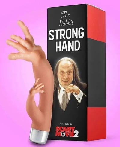 一张搞笑的恶搞产品图片，展示了一个名为"The Rabbit STRONG HAND"的玩具盒，盒子为黑红配色，上面印有一位长发男性的人像。盒子旁边伸出一只巨大的橡胶手模型，手的姿势夸张，手指张开，手掌向上。背景是鲜艳的粉红色，整体给人一种滑稽、荒诞的感觉。