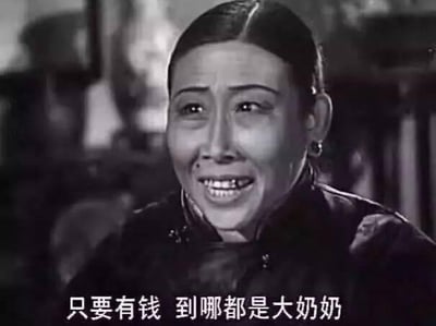 这是一张国产老黑白电影的剧照截图，图中是一位身着旧式服装的中老年女性，她脸上带着夸张、谄媚又市侩的表情，嘴巴大张，正急切地说着话。图下方配有字幕“只要有钱 到哪都是大奶奶”，直白地传递出一种金钱至上的市侩心态，常被网友用来调侃现实中那些将金钱等同于身份地位的人，没有双关、谐音梗等内容。