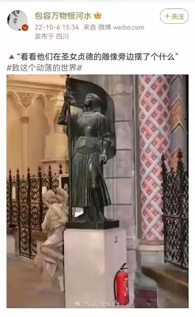 这是一张充满趣味的视觉错位实拍图，画面主体是一尊圣女贞德的立姿雕像，雕像的白色底座旁放置了一个红色灭火器。由于拍摄角度的巧合，灭火器的位置与雕像下半身重叠，看起来仿佛圣女贞德雕像的腿部变成了红色灭火器，制造出荒诞又搞笑的视觉效果。微博博主配文调侃“看看他们在圣女贞德的雕像旁边摆了个什么”，引发对这个巧合场景的趣味讨论。