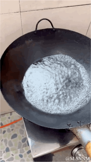 这是一段动态GIF，展示了一口放在炉灶上的黑色铁锅，锅里的白色粉末被晃动，看起来像是液体在剧烈沸腾，制造出逼真的“煮东西”假象，实则是利用视觉错位的趣味整活，反差感拉满，十分搞笑。