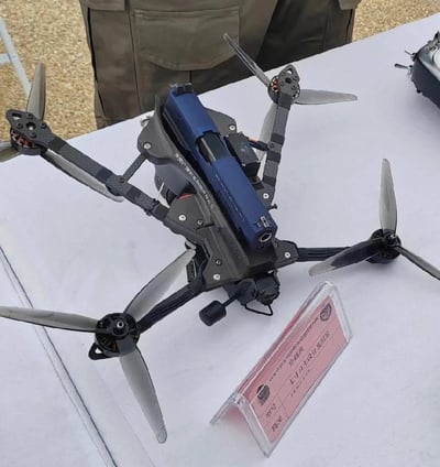 这是一张西安市公安局临潼分局巡特警支队展示的自主设计组装弩载四旋翼无人机的实拍图。无人机采用轻量化碳纤维机架，在机身中部搭载了一把改装制式弩具，弩具上印有合作厂商名称，旁边的透明展示牌标注了该装备的归属、类型与特点。整体结构紧凑专业，是针对特定警务需求改装的特种无人机，用于装备展示场景。