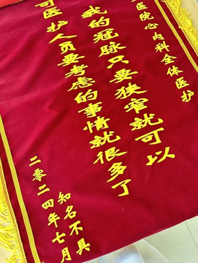 这是一面送给医院心内科全体医护人员的红色绒布锦旗，锦旗上用黄色立体字体印着特殊的感谢文案：“我的冠脉只要狭窄就可以 可医护人员要考虑的事情就很多了”，落款为“知名不具 二零二四年七月”。
文案用反向调侃的方式，看似降低自己的“要求”，实则是在共情医护人员工作的繁杂与不易，带着幽默又暖心的反差感，表达对心内科医护的理解与感谢。