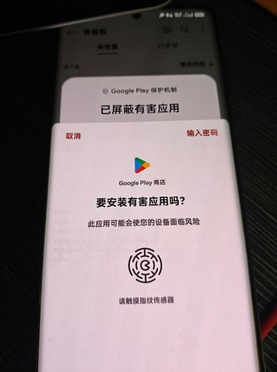 这是一张竖屏安卓设备的屏幕截图，展示了Google Play保护机制的安全提示场景：用户在尝试安装被判定为有害的应用时，系统弹出警示弹窗。弹窗顶部标注「已屏蔽有害应用」，核心区域由Google Play商店标识引出询问「要安装有害应用吗？」，并提示「此应用可能会使您的设备面临风险」，同时提供「取消」「输入密码」两个选项，底部还给出了指纹验证的引导。背景能看到设备的安装包管理页面，整体是系统为保护设备安全而触发的原生提示界面。