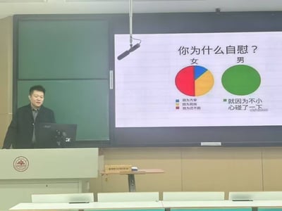 这张图片展现了一个大学教室或报告厅讲台场景，一人站在讲台前，而大屏幕显示着一张PPT，主题为“你为什么自慰？”。使用饼图对比男女自慰原因，女生有多个理由（如“因为寂寞”、“因为无聊”、“因为控不住”），而男生理由统一为“就因为不小心碰了一下”。该内容用调侃手法幽默表达两性差异，属于课堂或演讲PPT恶搞梗。图片风格轻松，自带自嘲和荒诞色彩，容易激发社交共鸣。