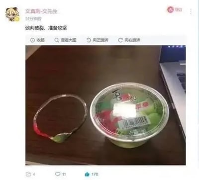这是一张社交媒体动态截图，发布者昵称为“文真则-文先生”，头像是Q版动漫角色，发布文案为“谈判破裂，准备攻坚”。配图是桌面场景，右侧放着一杯未开封的杯装果冻，塑封膜完好，左侧是已经被撕下来、但没有连带扯下果冻封膜的塑料撕拉条。创作者将撕果冻盖失败的小事夸张类比为谈判破裂，把接下来要打开果冻的行为调侃为“攻坚”，用夸张的军事化话术赋予普通生活小事极强的戏剧性，趣味性十足。