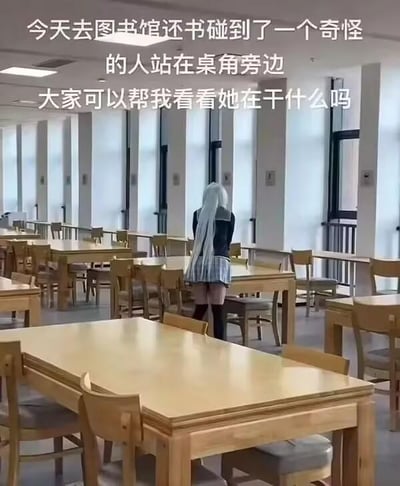 这是一张在图书馆内拍摄的趣味照片，利用视角巧合制造出视觉错位效果。图上方的文字写着“今天去图书馆还书碰到了一个奇怪的人站在桌角旁边 大家可以帮我看看她在干什么吗”，引导观众观察。实际上这是视觉错位的效果，画面里看起来像是银灰色长发女孩站在桌角，实际是一个人坐在椅子上，她的头发和桌角的视角巧合营造出了这个有趣的错觉，带来搞笑新奇的观感。