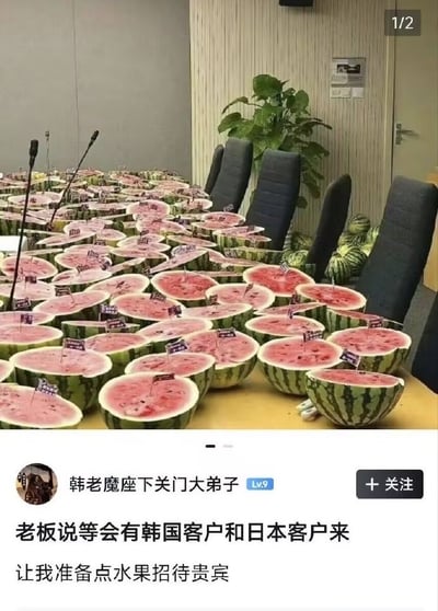 整张图为图文混排的社交媒体截图，上半部分拍摄的是常规会议室的长桌桌面，原本应摆放会议资料的位置被密密麻麻的对半切开的西瓜铺满，每半块西瓜上都插有迷你小旗子，会议桌一侧的椅子旁还堆放着数个完整的西瓜，桌面设有会议麦克风，背景可见墙面绿植与办公座椅，是标准的商务接待场景布置；下半部分是发帖用户的发言，用户昵称为“韩老魔座下关门大弟子”，账号等级Lv9，配文说明老板要求自己准备水果招待即将到访的韩国、日本客户，而自己准备了满桌西瓜。该内容的笑点在于韩国与日本的生鲜物价较高，西瓜属于价格昂贵的日常水果，用满桌西瓜招待客户属于超出常规的“高规格”接待，带有调侃整活的趣味效果。