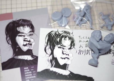 这张图展示了一套同人创作的哥特风格恶魔少女GK（未涂装树脂手办）套件，包含两张角色设定插画：插画中的少女扎着高马尾、长着恶魔角，身着哥特洛丽塔服饰，双臂抱于胸前，表情冷漠略带不悦；同时还有多个灰色未涂装的树脂白模，其中包含造型怪异的双人扭打类小模型，以及一张手写日文感谢卡，卡上文字意为“非常感谢您购买了很多”，整体是手办爱好者购入自制套件后的展示场景。