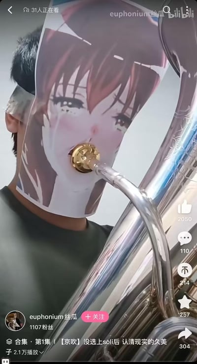这是B站用户的整活视频截图，创作者将《吹响！上低音号》里的角色黄前久美子的哭泣表情立牌贴在脸上，让上低音号的号嘴恰好对准立牌的嘴部，制造出“久美子在吹上低音号”的视觉错位效果，结合视频标题的玩梗，趣味十足。
无谐音梗或双关，核心是视觉错位带来的搞笑感。