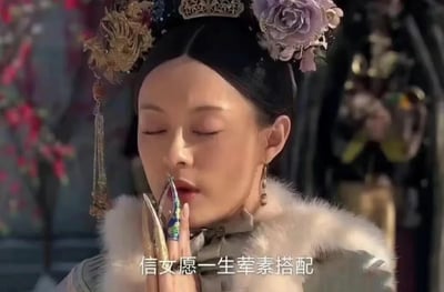 图片为《甄嬛传》中甄嬛的经典剧照改编，她身着带有毛领的古装服饰，头戴精致的金色头饰与紫色花朵，双手合十闭眼作祈祷状，画面底部配有文字“信女愿一生荤素搭配”。这是对原版“信女愿一生吃素”梗的搞笑升级，通过将“吃素”改为“荤素搭配”，幽默体现了当代年轻人“想要好运又不想严格付出代价”的矛盾心理和自嘲精神。