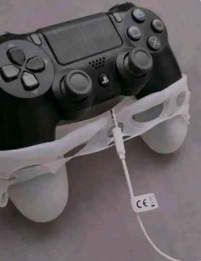 这是一张充满脑洞的创意摆拍图，主体是一台黑色的索尼PS4 DualShock 4游戏手柄。创作者用白色的口罩将手柄的两个握把部分捆绑起来，同时在手柄的耳机接口处插入了一根白色的3.5mm耳机线，耳机线上带有CE认证标识的标签清晰可见。通过物品的巧妙组合与摆放，让原本冰冷的游戏手柄被拟人化，看起来像是一个戴着口罩、连接着“吸氧管”的病人，利用视觉错位的效果营造出荒诞搞笑的趣味氛围，很容易引发游戏玩家的共鸣，用来调侃长时间游戏后的疲惫状态。
